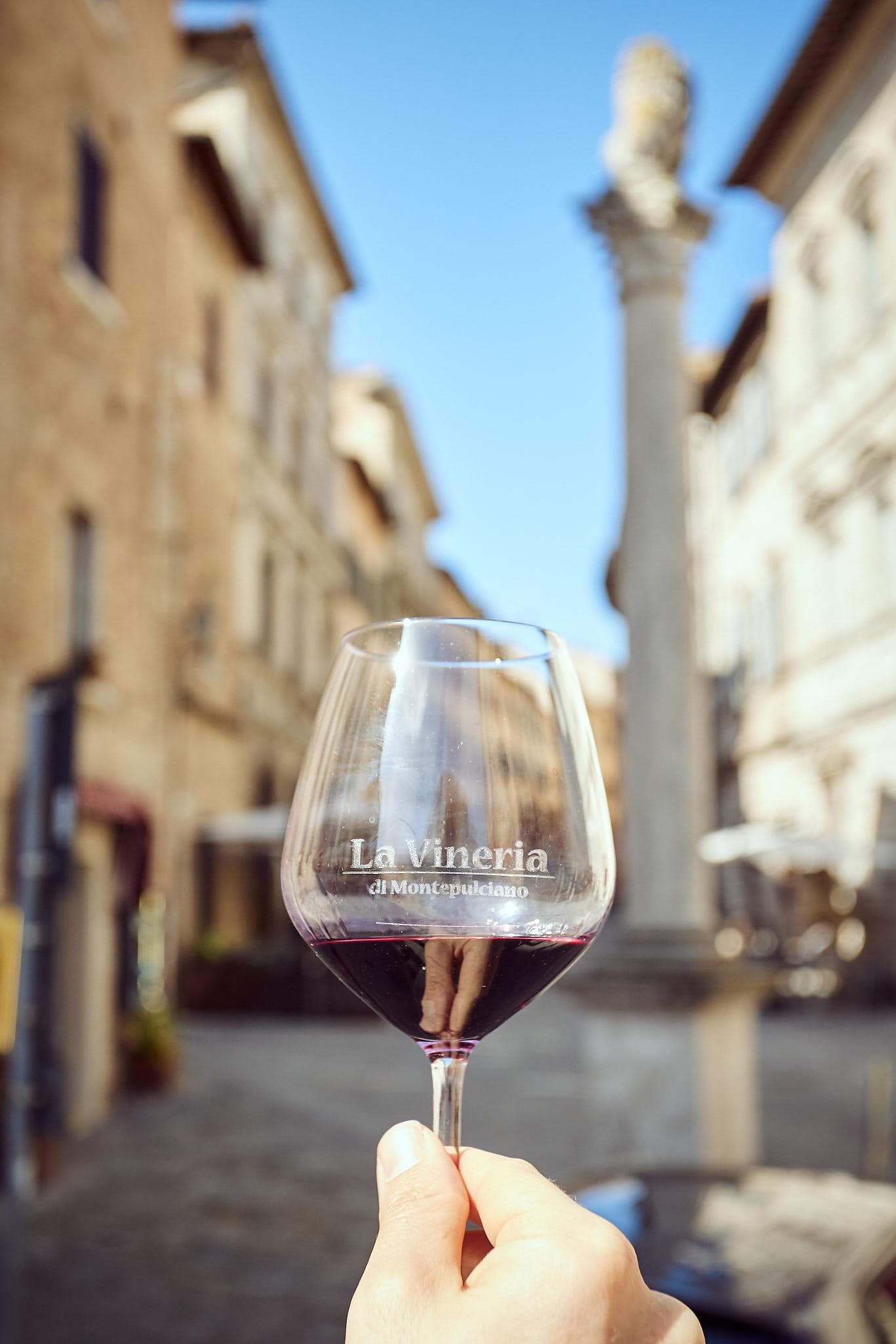 Un calice inciso con il nome della Vineria, riempito di vino rosso in mezzo alla via