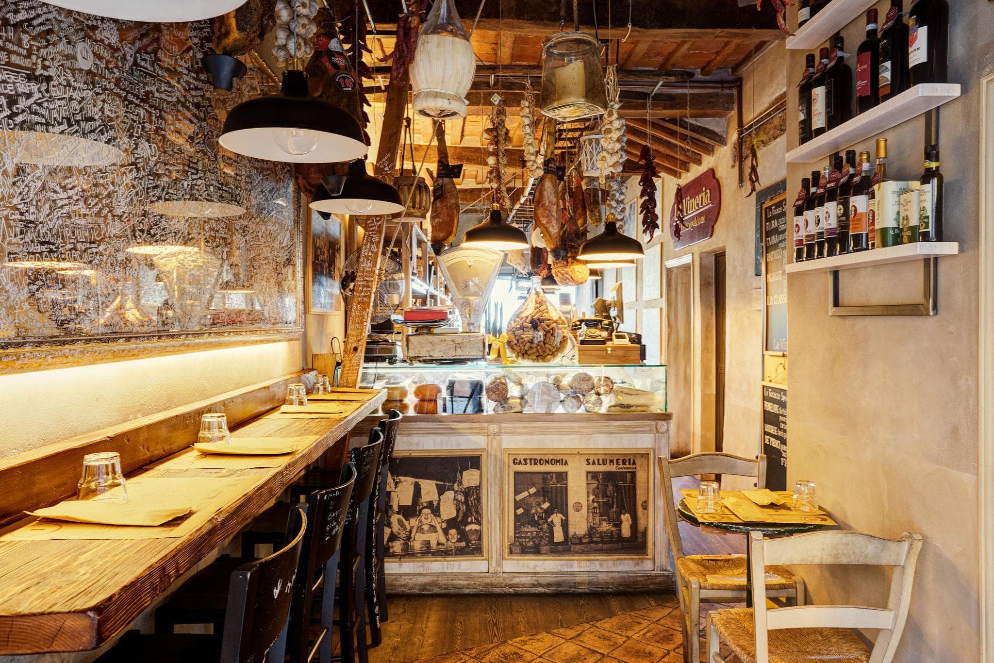 Il bancone della Vineria, con i salumi appesi e le lampade accese sopra il ripiano di legno